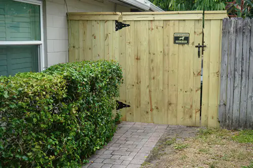 Board on board wood gate with a cap rail and black strap hinges beside a paver walkway in Orlando, next to an older weathered fence