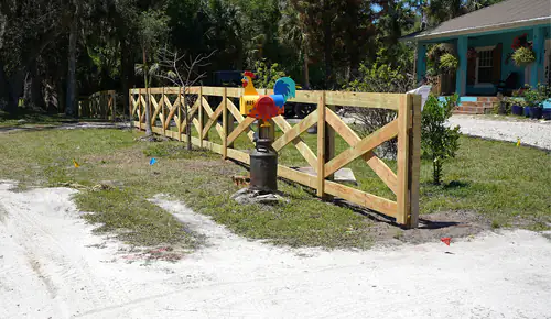 Pressure treated crossbuck wood fence with X braced sections across the front yard of a teal cottage in New Smyrna Beach