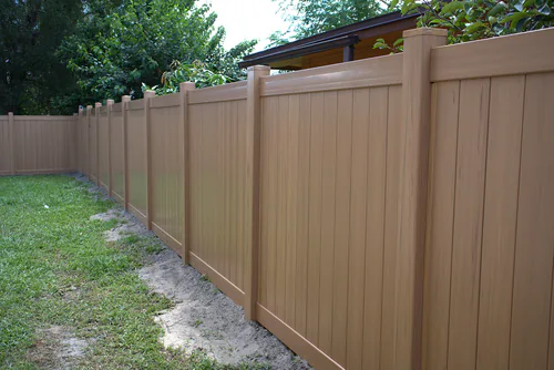 Cypress woodgrain vinyl privacy fence running along a Longwood back yard property line with a fresh soil trench along its base