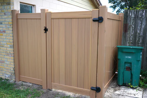 Cypress vinyl walk gate with black self latching hardware fitted between a brick house wall and an existing weathered wood fence in Longwood