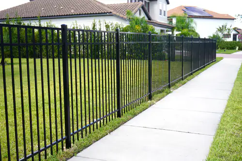 Black aluminum fence running along a public sidewalk past tile roofed homes in a DeBary neighborhood