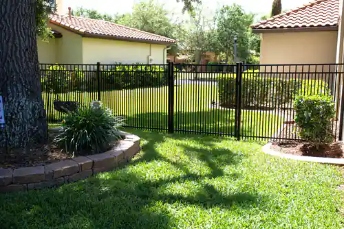 Black double picket aluminum fence and gate in a DeBary community with tile roofed homes and a paver planting bed behind it