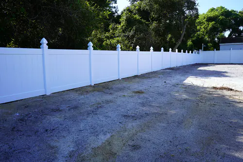 Four foot tall white vinyl fence with decorative post caps curving along the edge of a cleared Deltona lot