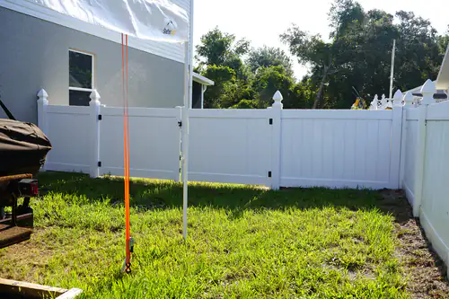 White vinyl fence panels beside a Deltona home with an orange utility locate marker and a string line set for the post tops