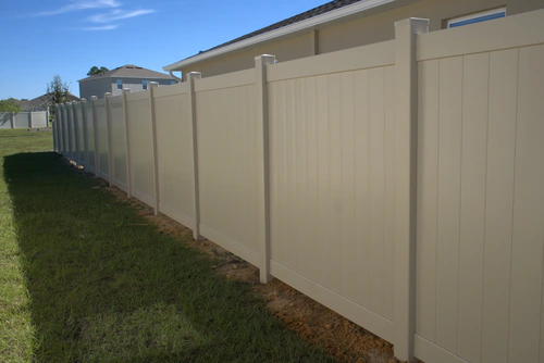 Tan vinyl privacy fence running from the side of a new construction home in Winter Garden with clay backfill along the base of the panels