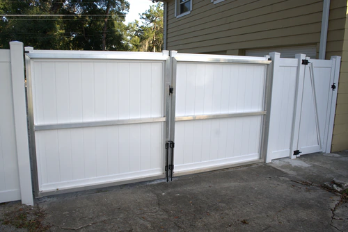 White vinyl double drive gate with a galvanized aluminum frame closed across a concrete driveway in Longwood