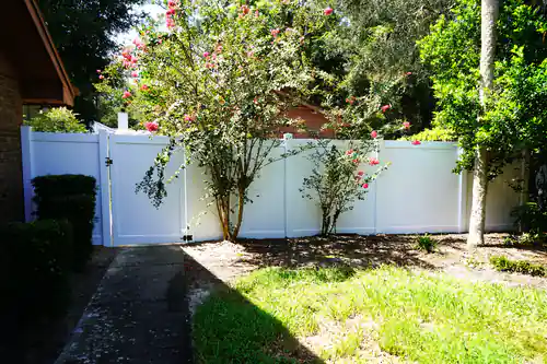 White vinyl privacy fence and walk gate running beside a Deltona home with a blooming crepe myrtle in front of it